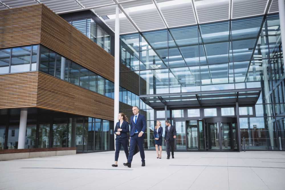 Facility managerek öltönyben egy modern irodaház előtt, ügyfelekkel egyeztetve