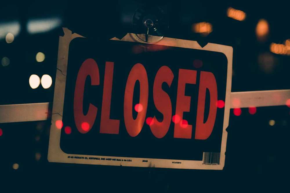 Bezárt üzlet ajtaján lógó ‘Closed’ tábla éjszakai fényekkel a háttérben.